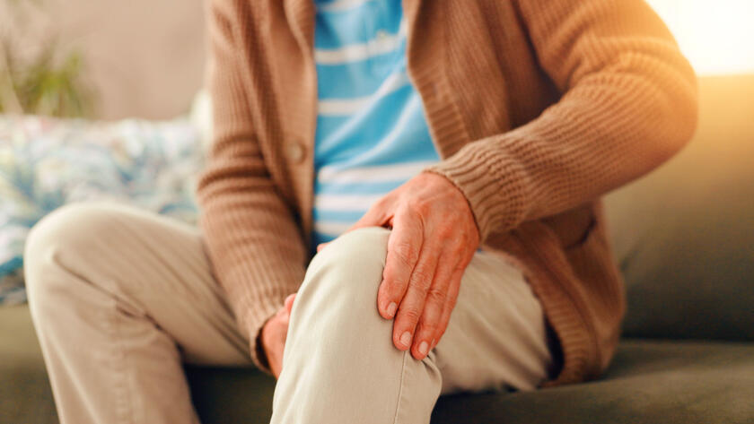 Older person sitting on a couch holding their knee due to joint pain