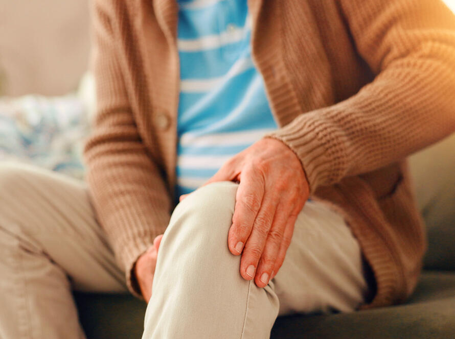 Older person sitting on a couch holding their knee due to joint pain