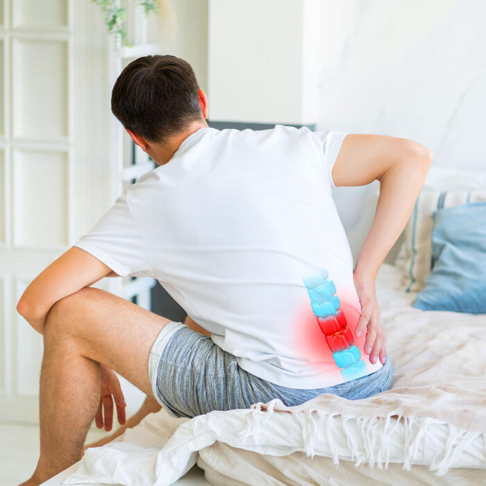 Man sitting on bed holding lower back in visible pain