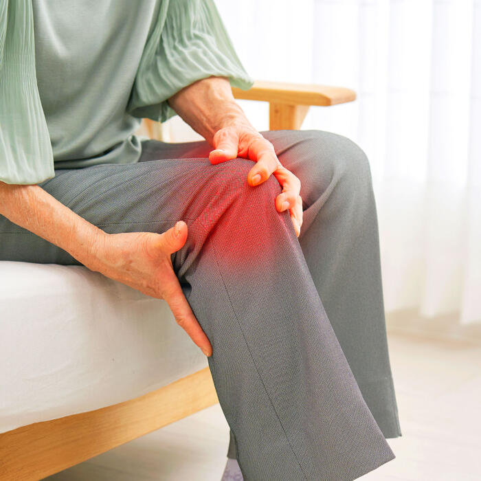 Senior man gripping painful knee joint while sitting on bed