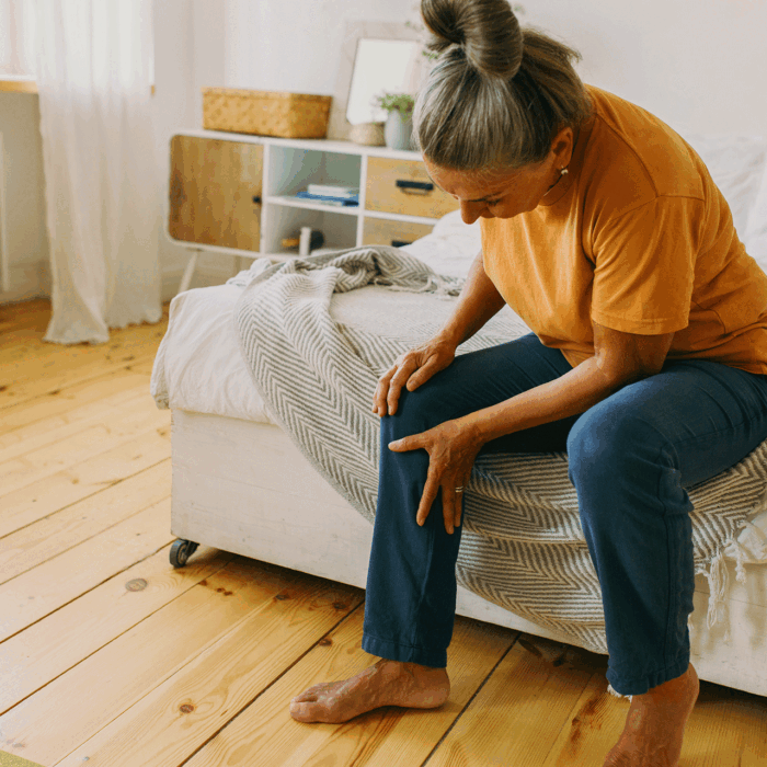 Senior woman sitting on a bed and holding her knee due to joint pain.