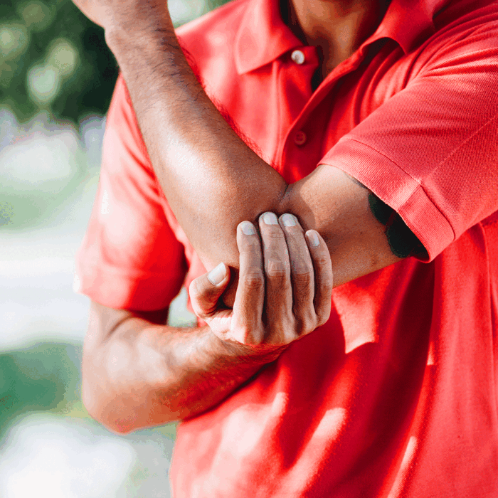 Close-up of a man holding his elbow in pain outdoors.